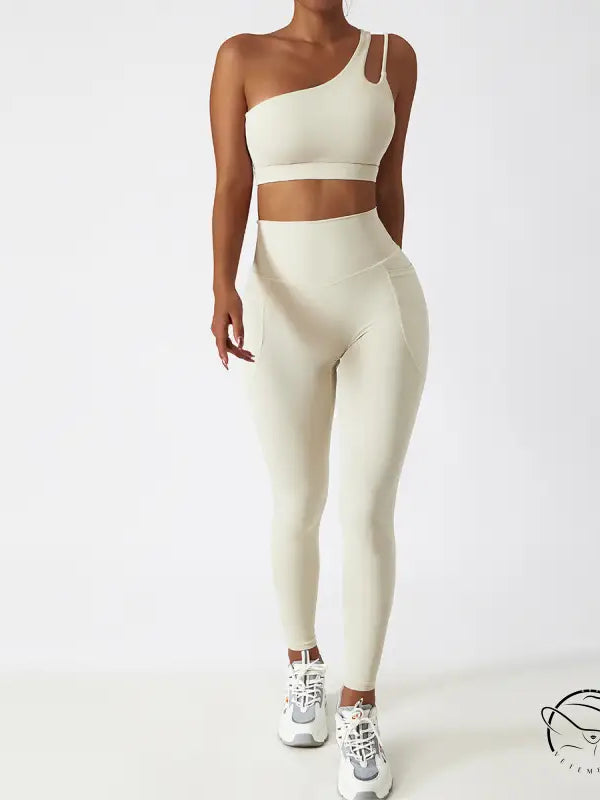 Cream-colored one-shoulder sports bra and high-waisted yoga pants set with white sneakers