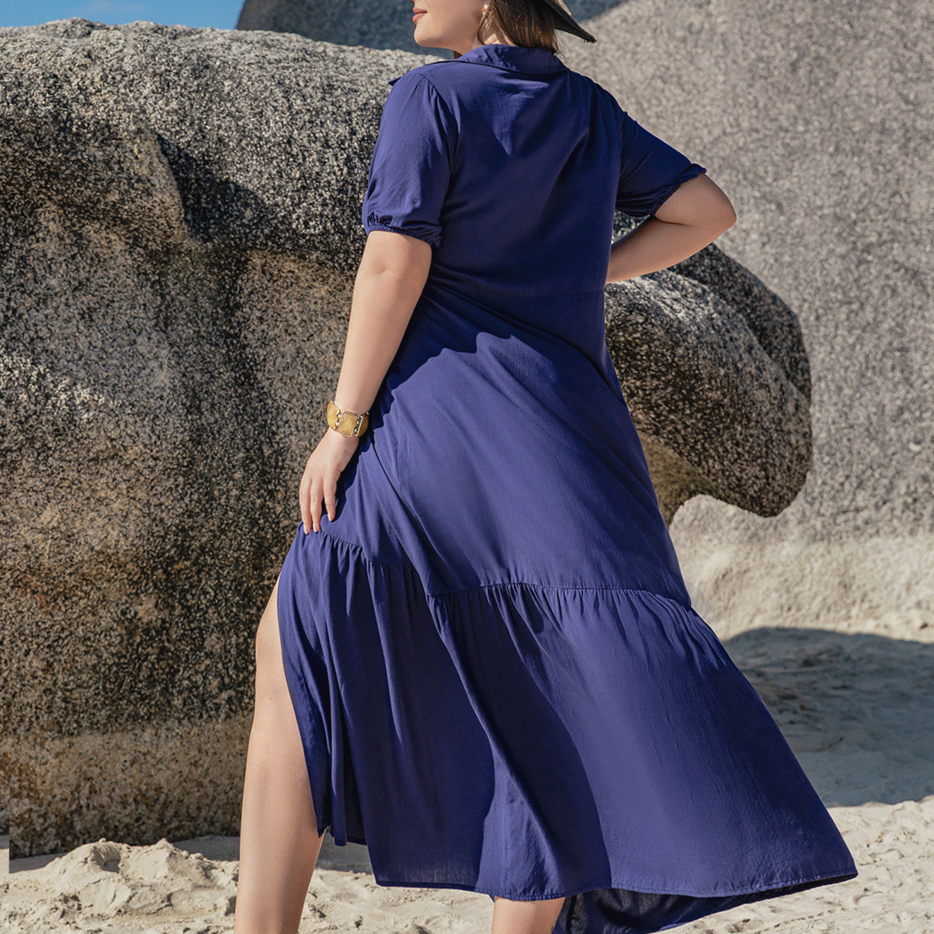 Woman in dark blue Bohemian mixed batch loose dress with high slit, hat, and gold bracelet