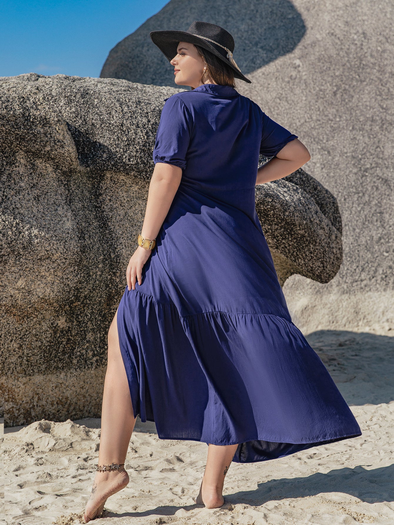 Woman in dark blue Bohemian mixed batch loose dress with high slit, hat, and gold bracelet