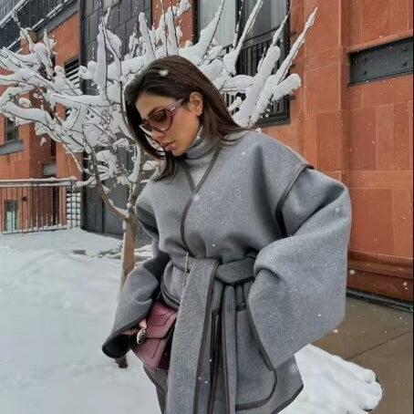 Elegant woman in gray belted cape coat with maroon handbag showcasing fashionable ملابس