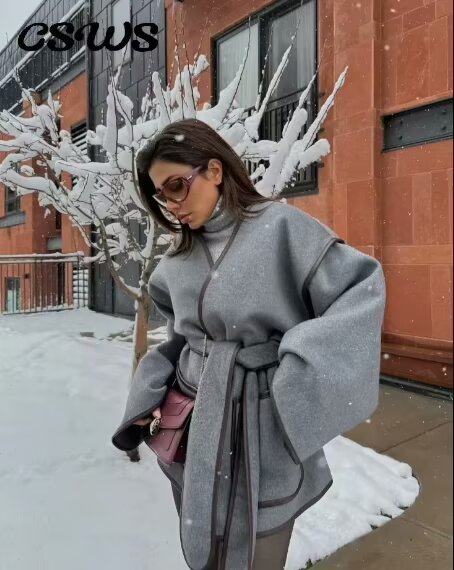 Elegant woman in gray belted cape coat with maroon handbag showcasing fashionable ملابس