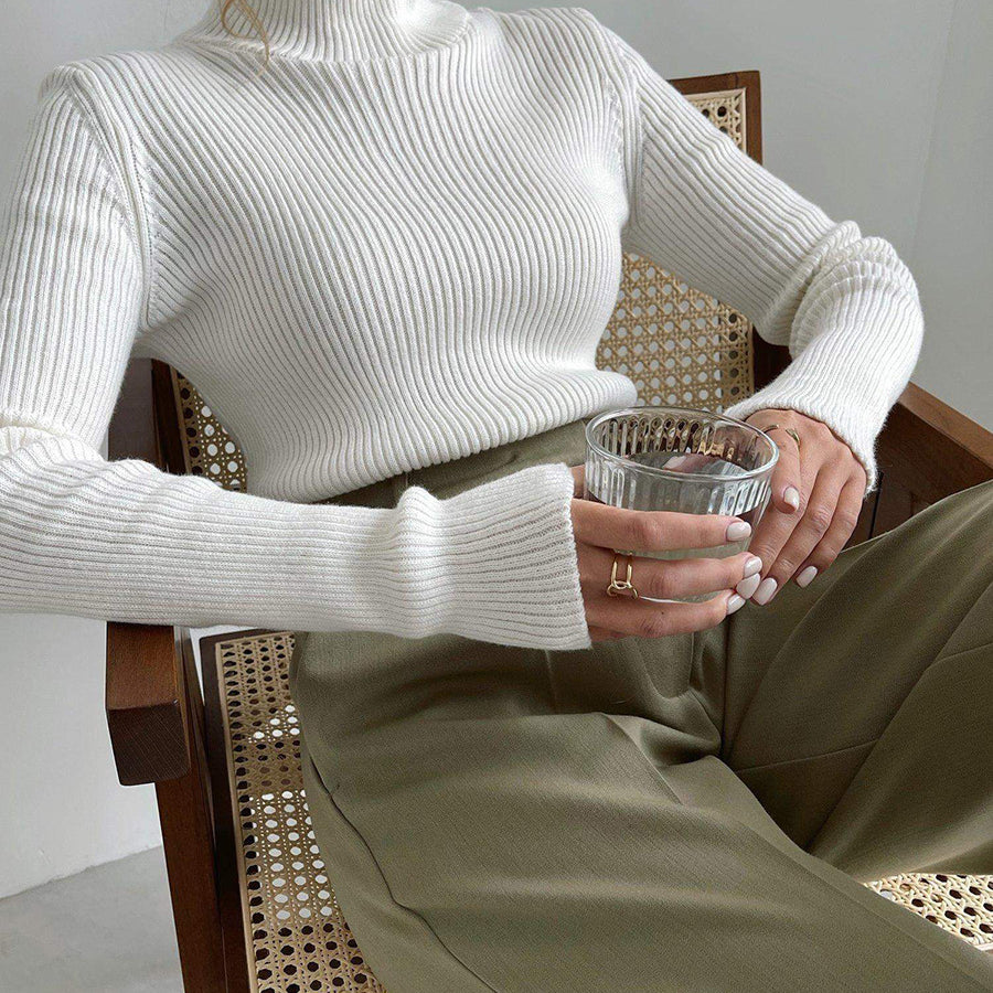 Langry fashion white ribbed turtleneck sweater with olive green pants on perforated chair