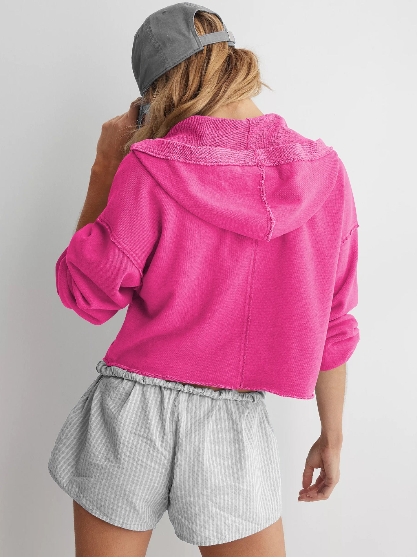Hot pink cropped hoodie styled with gray striped shorts and a baseball cap, langry fashion