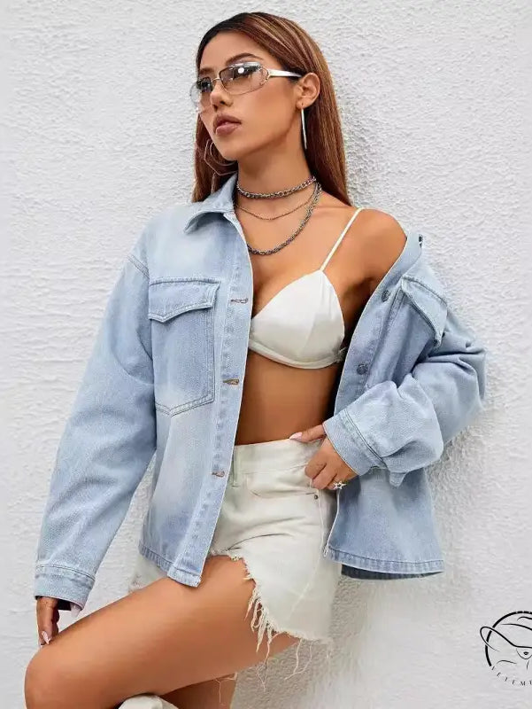 Fashionable woman in loose langry denim coat, white bralette, and distressed shorts