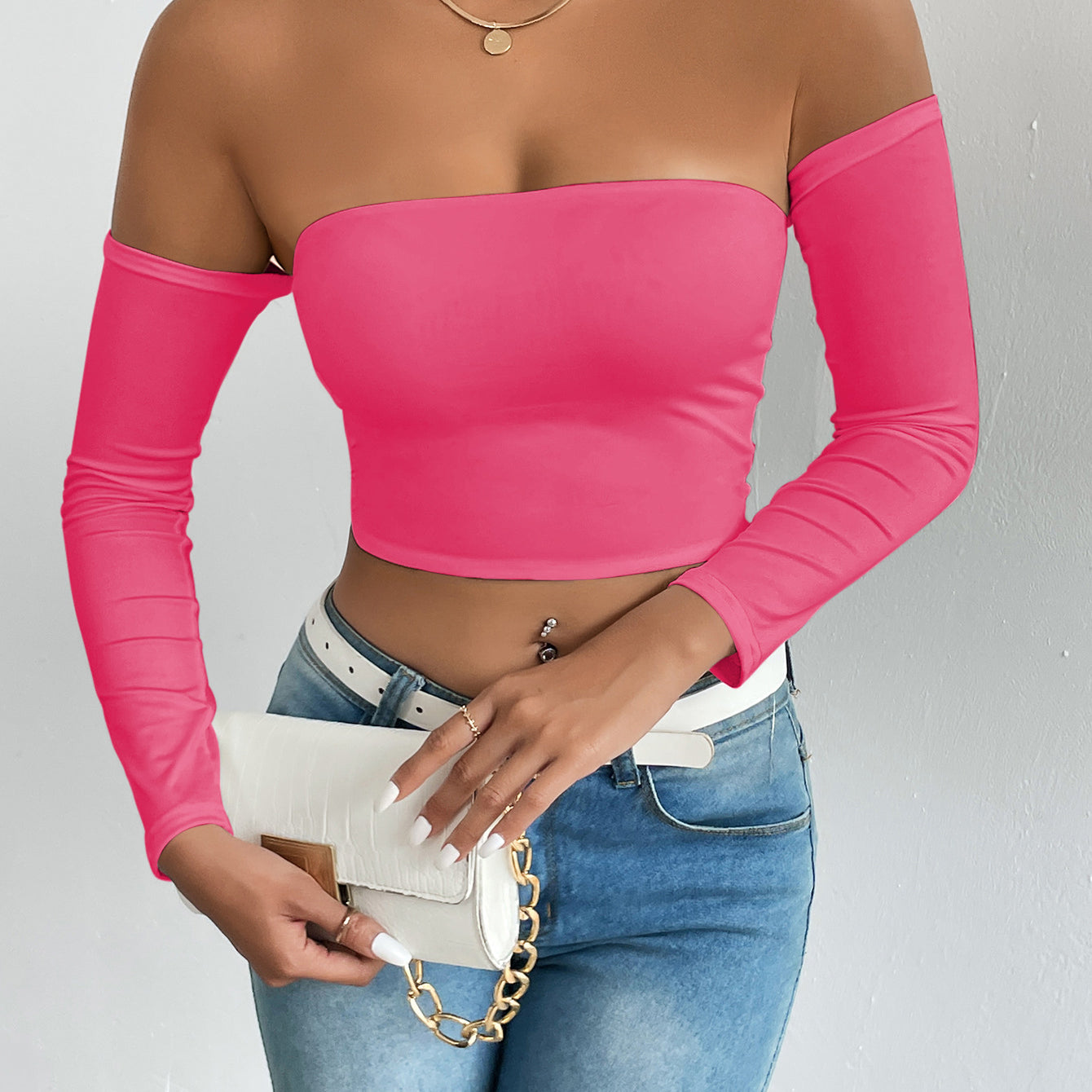 Hot pink off-the-shoulder crop top with light-wash jeans, white belt, and handbag