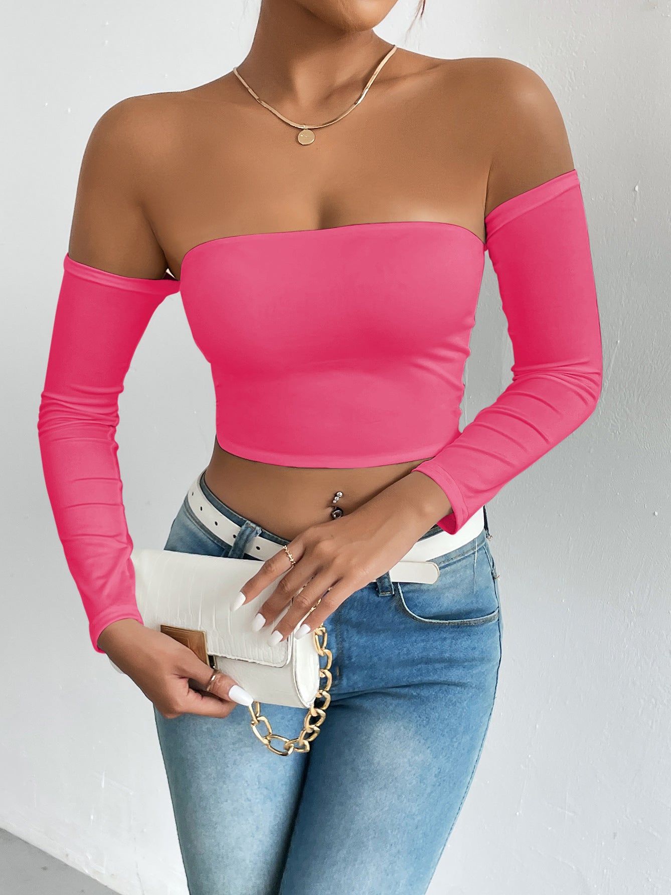 Hot pink off-the-shoulder crop top with light-wash jeans, white belt, and handbag