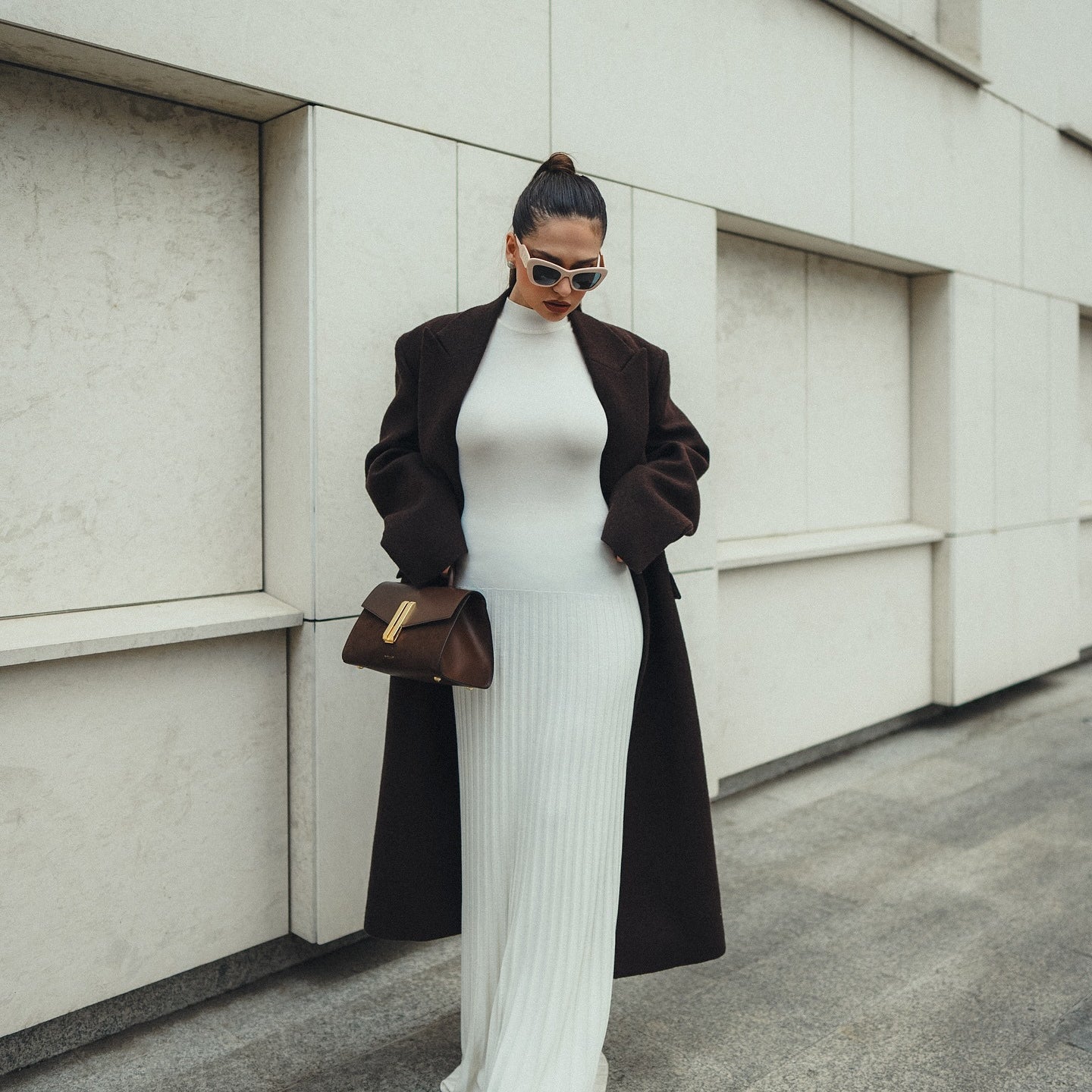 Elegant white bodycon maxi dress with a long black coat and brown handbag in fashion