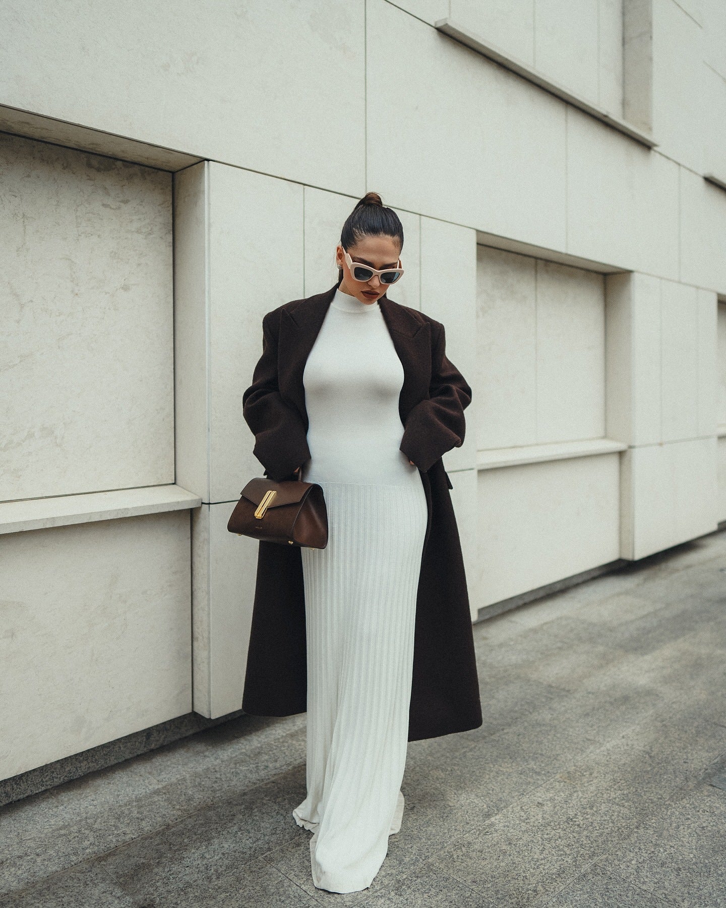 Elegant white bodycon maxi dress with a long black coat and brown handbag in fashion