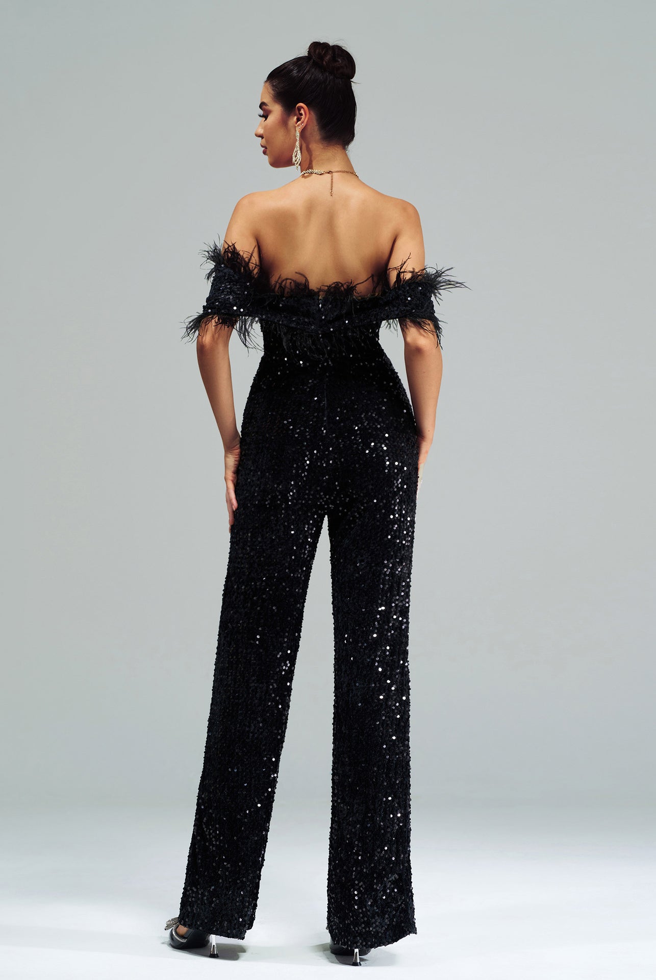 Elegant sequin-covered black jumpsuit with feather trim showcasing high-end fashion style