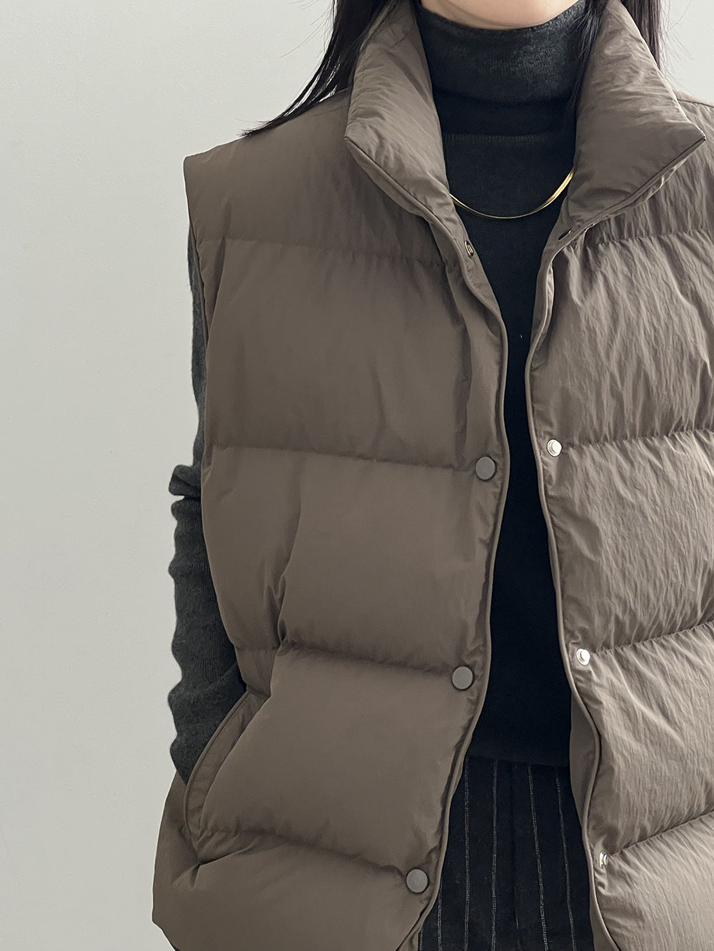 Taupe quilted puffer vest with snap buttons over black top in Langry fashion ملابس