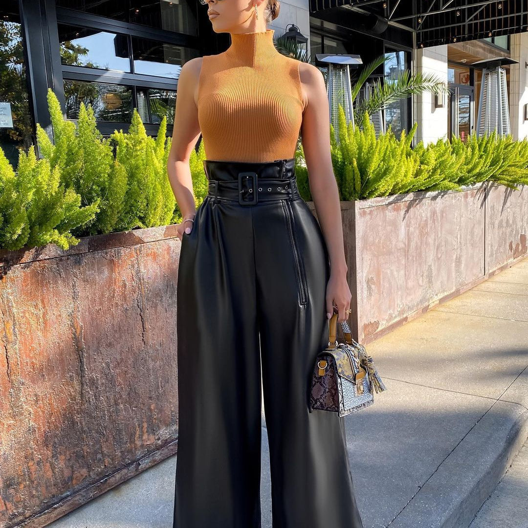 Woman in mustard yellow turtleneck and high-waisted faux leather pants holding a patterned handbag