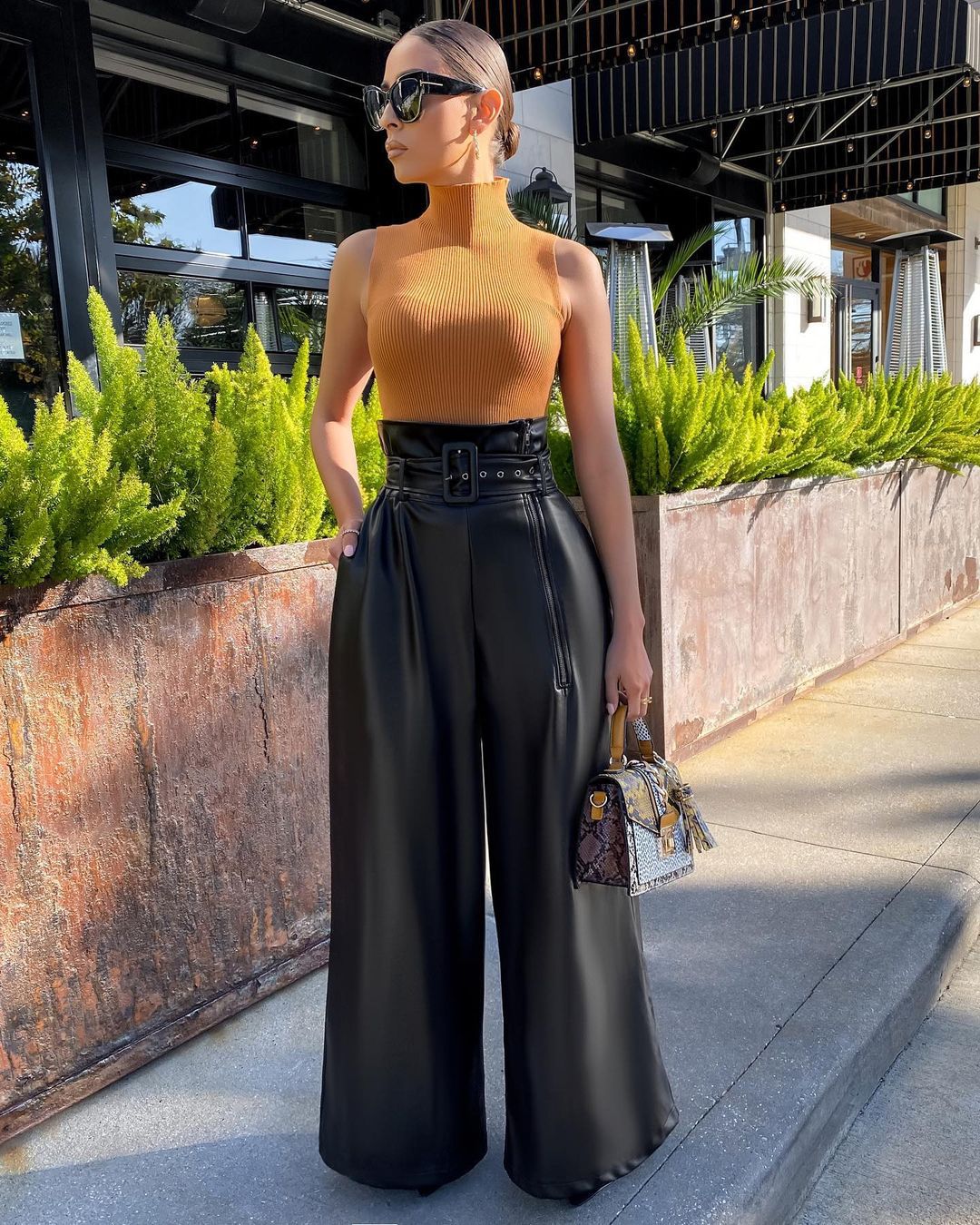 Woman in mustard yellow turtleneck and high-waisted faux leather pants holding a patterned handbag