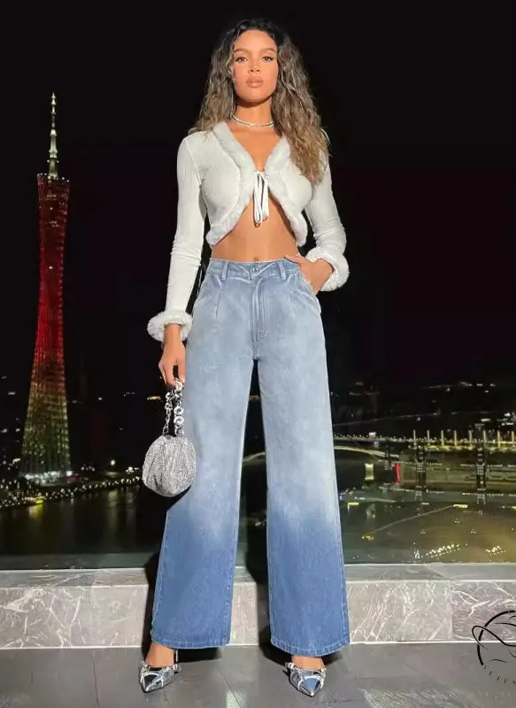 Woman in white fluffy crop top and high-waist denim trousers holding silver handbag