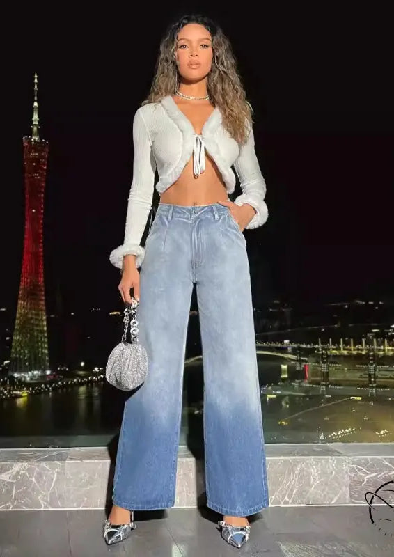 Woman in white fluffy crop top and high-waist denim trousers holding silver handbag