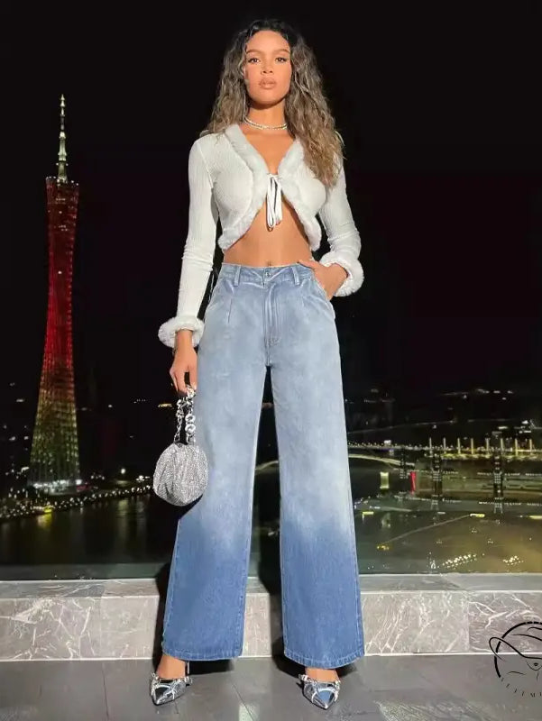 Woman in white fluffy crop top and high-waist denim trousers holding silver handbag