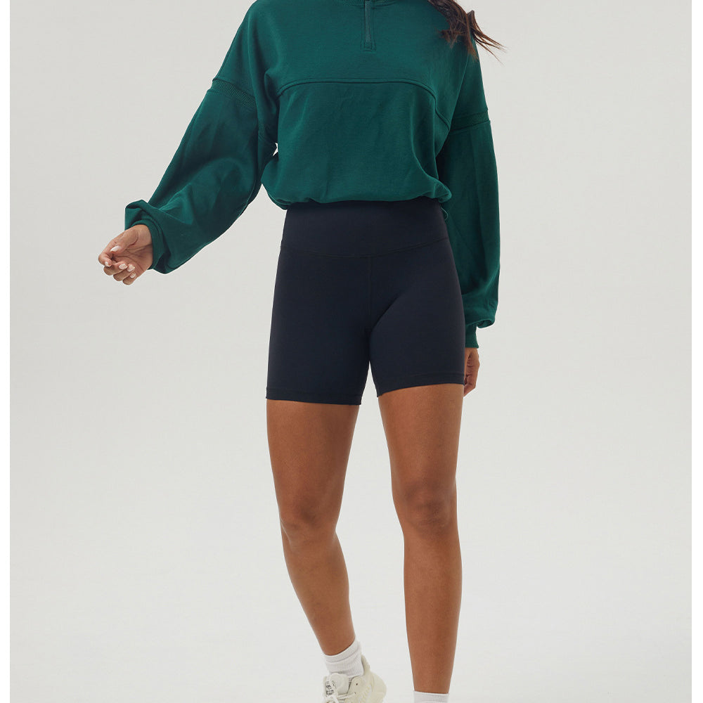 Woman in green long sleeve sweatshirt and black shorts, showcasing casual fitness fashion