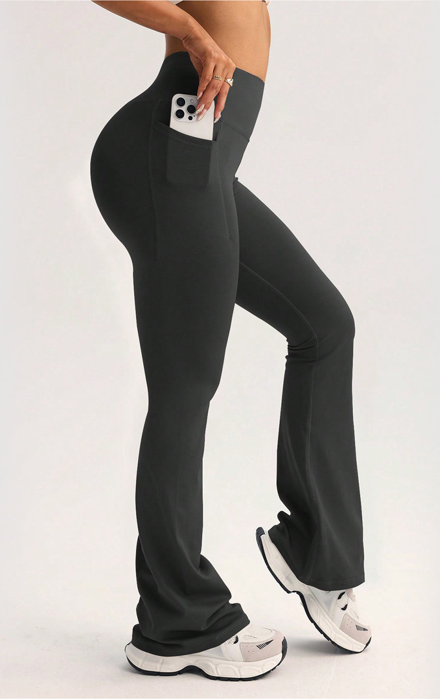 Black langry high-waisted flared yoga pants with side pocket holding white smartphone
