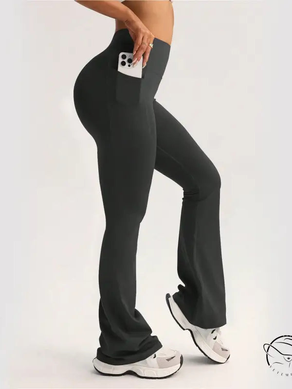 Black high-waisted flared langry yoga pants with side pocket holding white smartphone