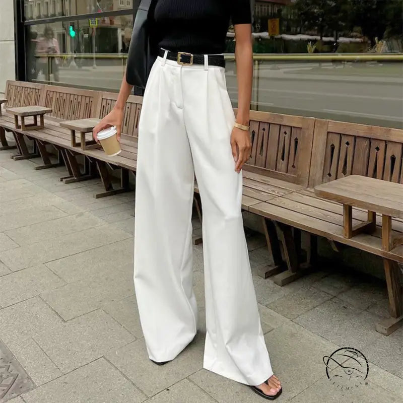 Person in pure white office trousers, black top, belt, sandals, holding coffee