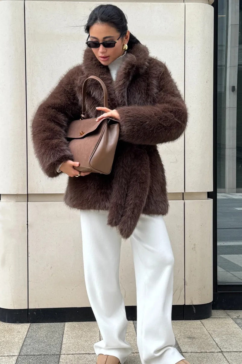 Brown faux fur coat with white pants and tan handbag in Langry fashion