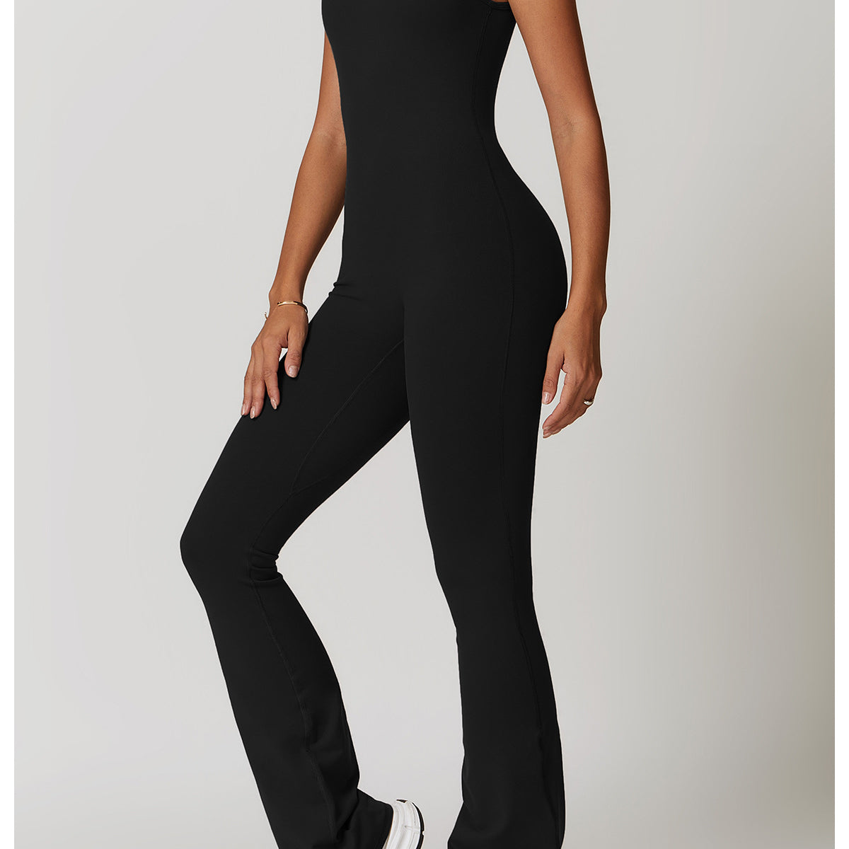 Black sleeveless athletic jumpsuit with flared legs and white sneakers for yoga fashion