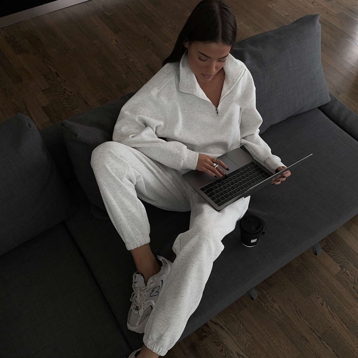 Woman in gray sweatsuit using laptop, showcasing Langry fashion for casual comfort