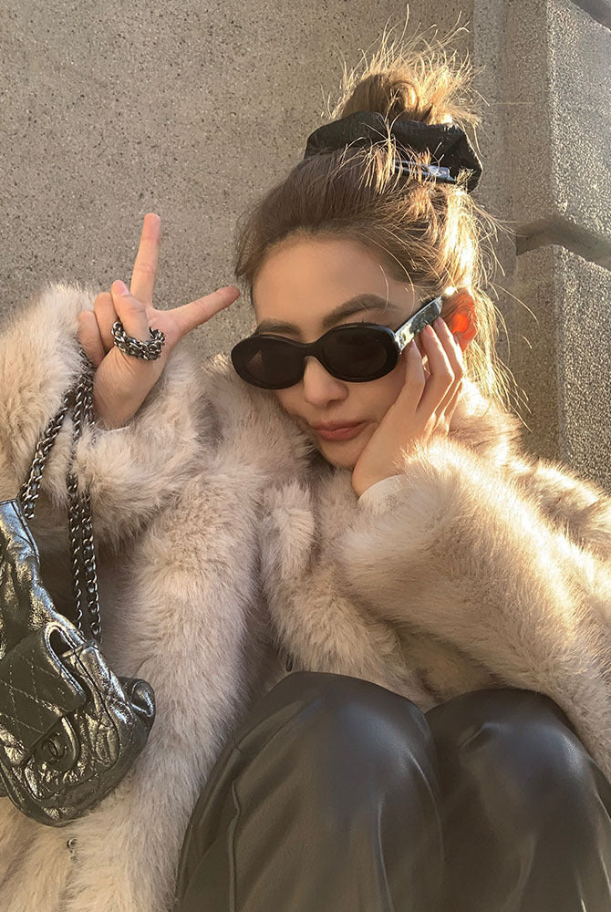 Cream faux fur coat with black sunglasses and silver chain bag