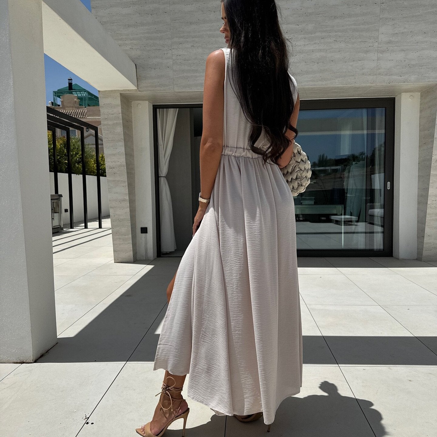 Woman in a long, light-colored V neck split sleeveless dress showcasing elegant fashion style