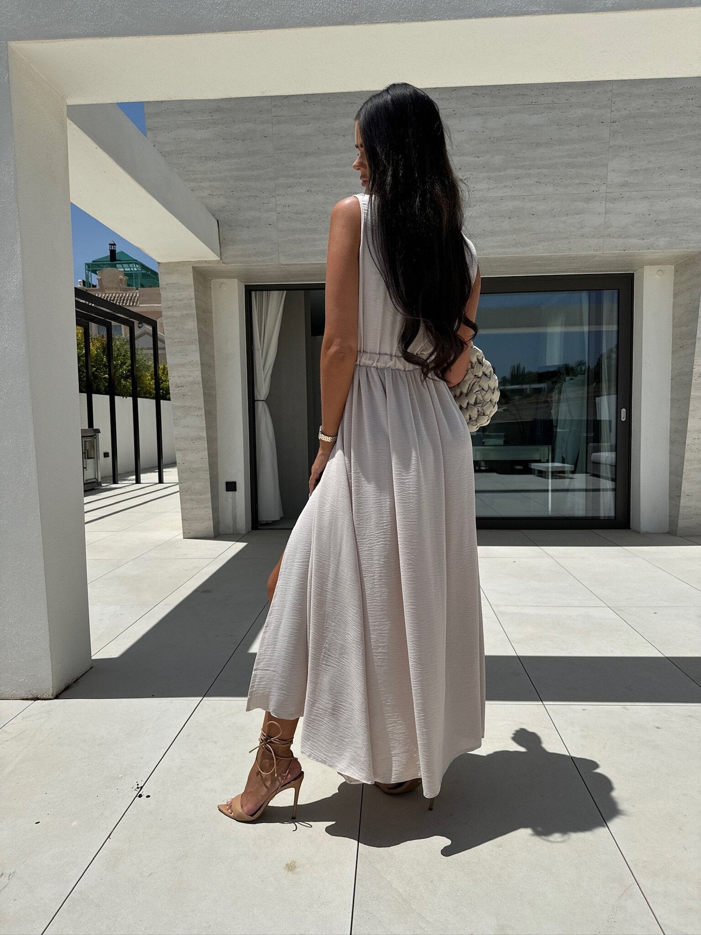 Woman in a long, light-colored V neck split sleeveless dress showcasing elegant fashion style