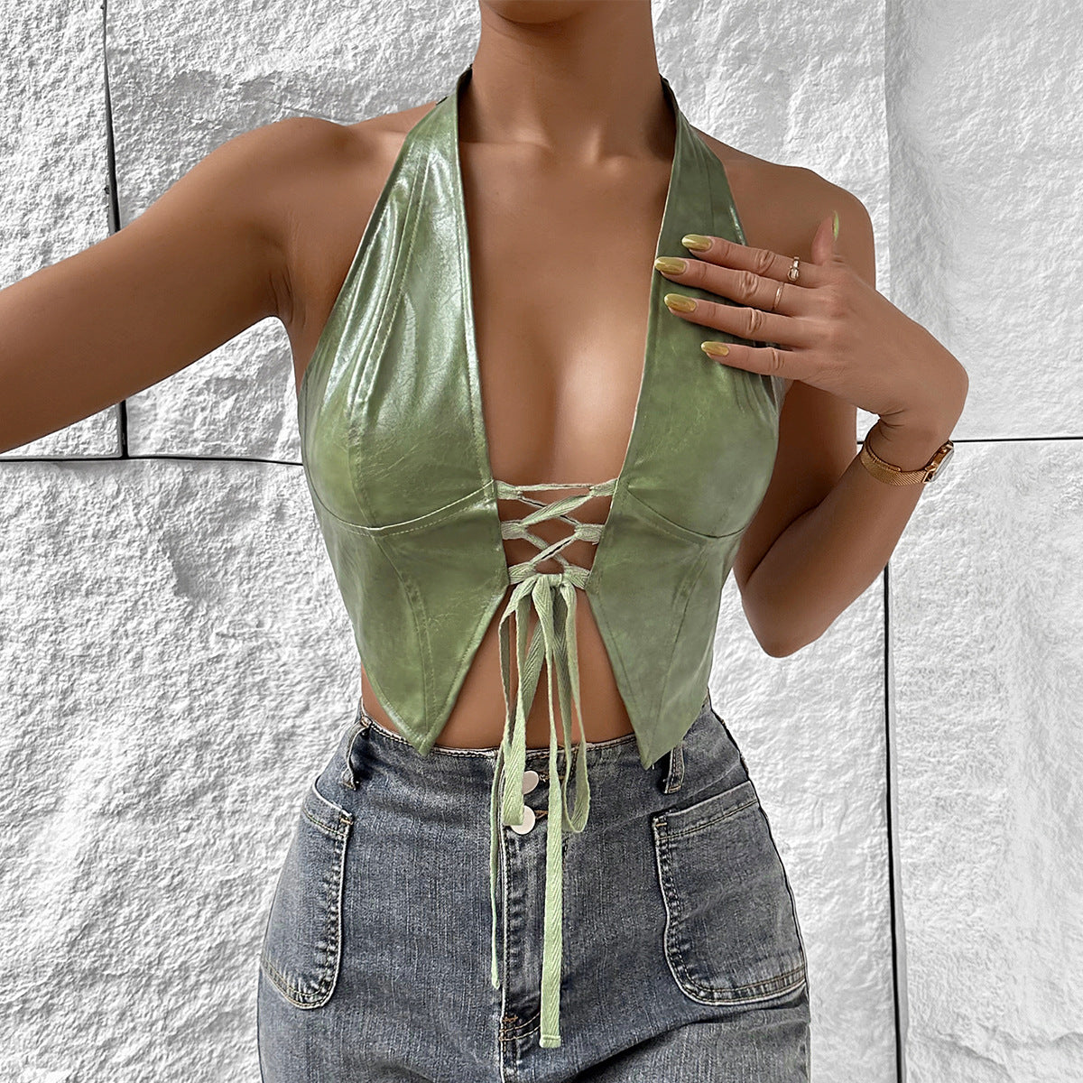 Woman wearing a shiny light green solid color halter top with lace-up front and dark jeans