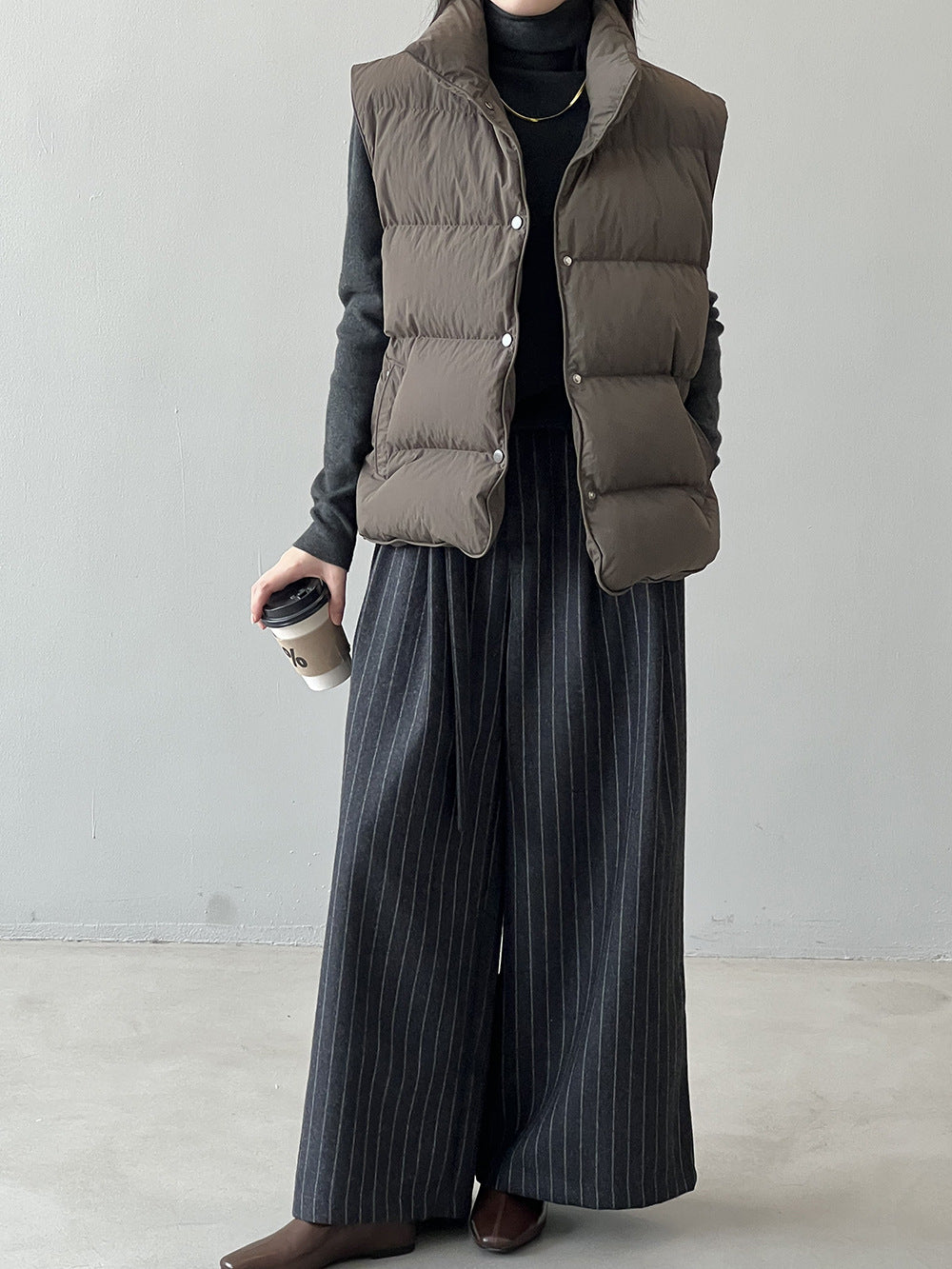 Taupe puffer vest styled with black turtleneck and pinstriped pants, perfect for fashion ملابس