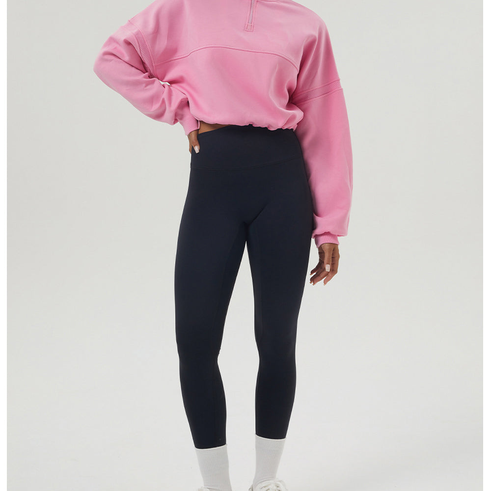 Woman in pink long sleeve sweatshirt and black leggings showcasing fitness fashion style