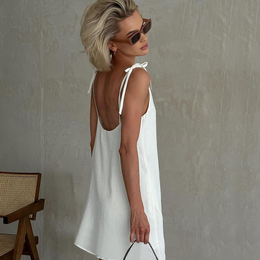 Woman in white slip dress with tie-shoulder straps and sunglasses, stylish summer fashion