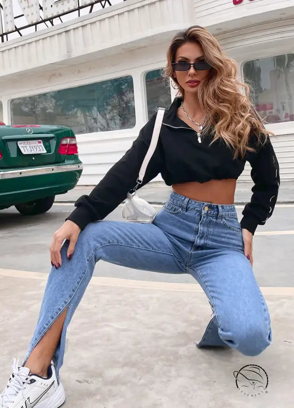 Young woman in black crop-top and langry high-waist denim pants with split hems