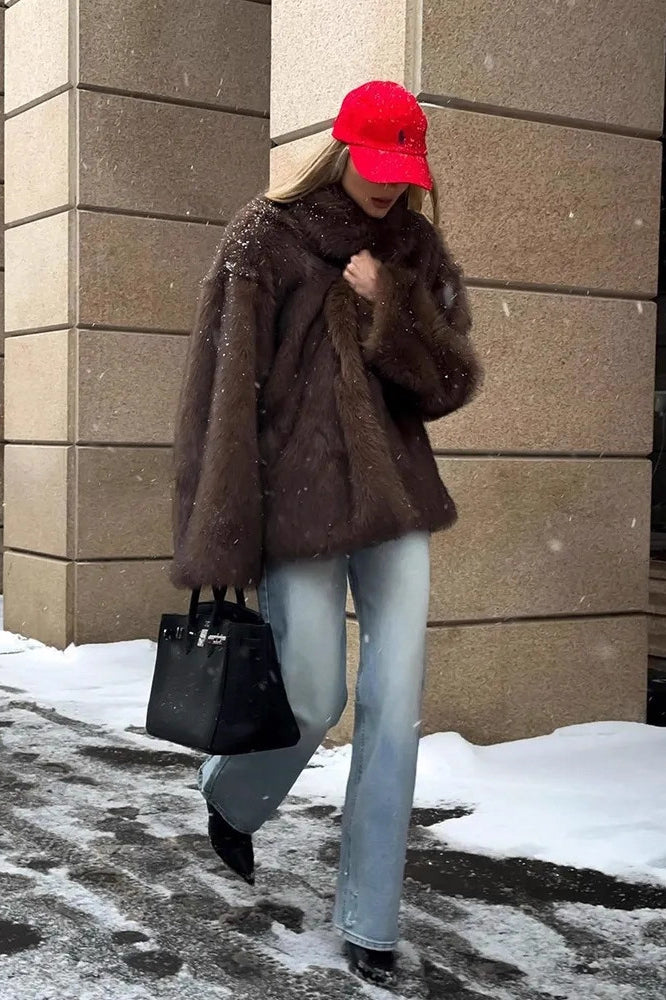 Fashionable warm faux fur coat with black leather handbag and silver hardware