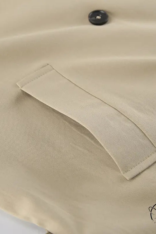 Beige trench coat with button-down shirt pocket and black button detail