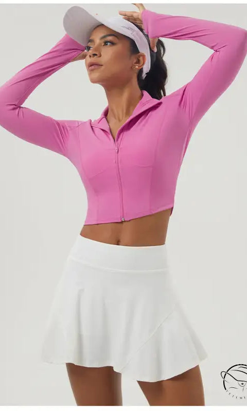 Woman in long sleeve pink zipper sports jacket and white pleated tennis skirt