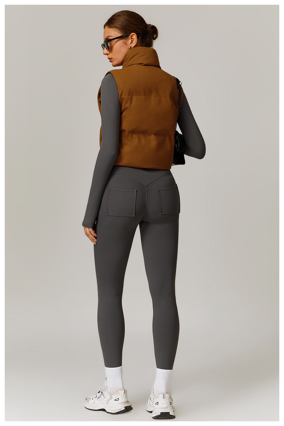 Woman wearing stylish brown puffer vest and gray leggings, perfect for winter fashion
