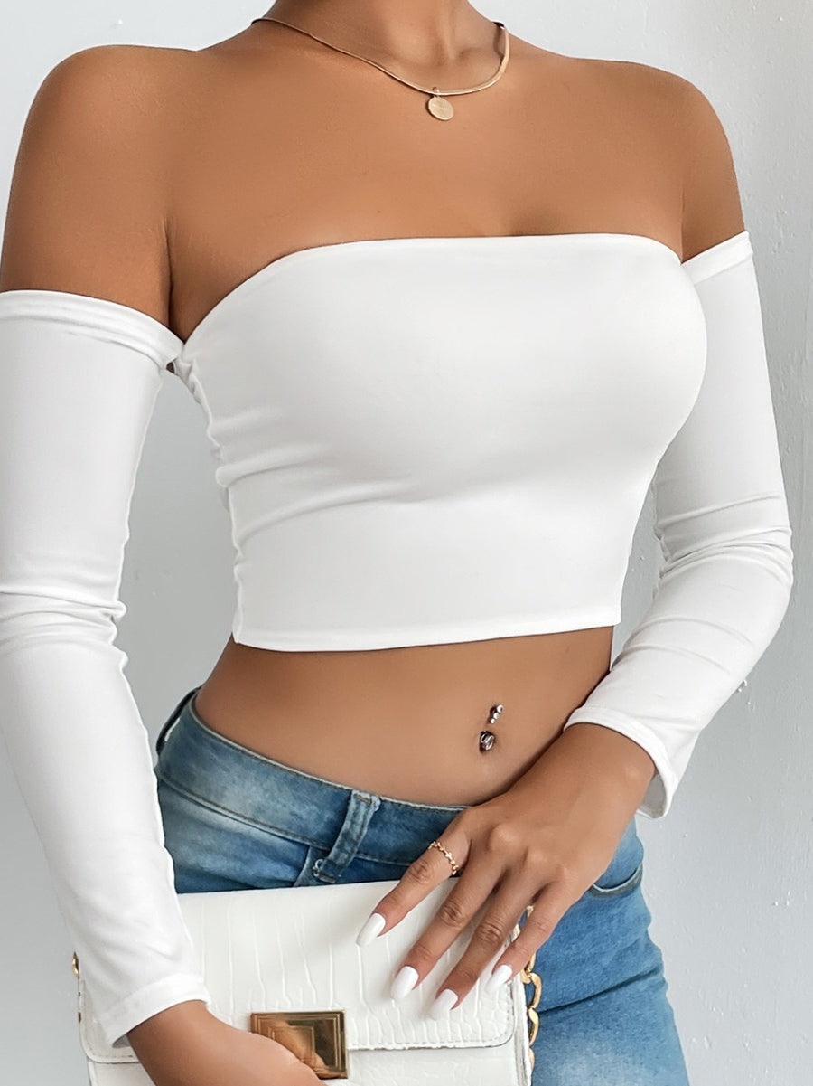 Fashionable woman wearing white off-shoulder crop top with blue jeans and white handbag