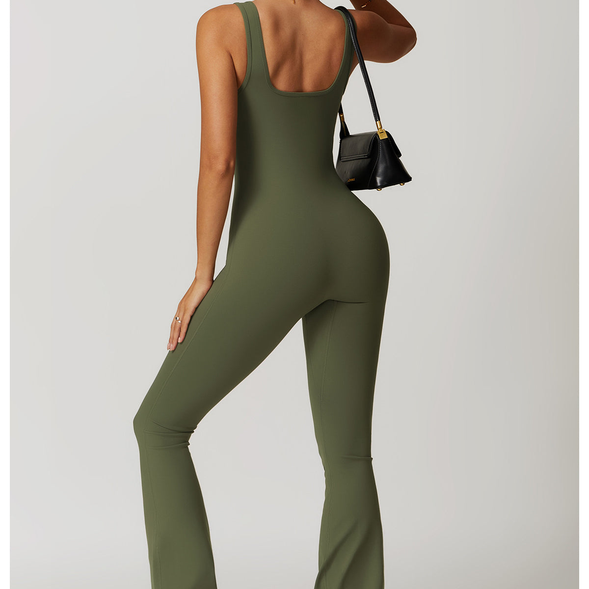 Olive green sleeveless jumpsuit with flared legs, white sneakers, and black handbag in fashion