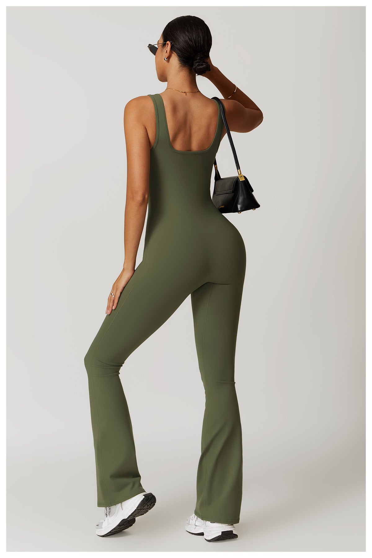 Olive green sleeveless jumpsuit with flared legs, white sneakers, and black handbag in fashion