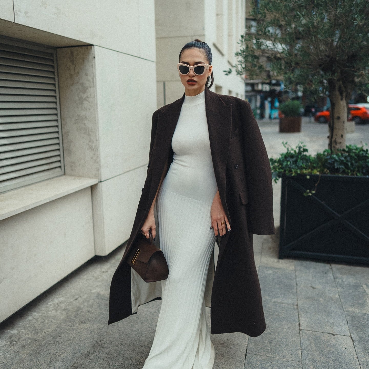 Elegant white bodycon maxi dress styled with a long black coat and sunglasses