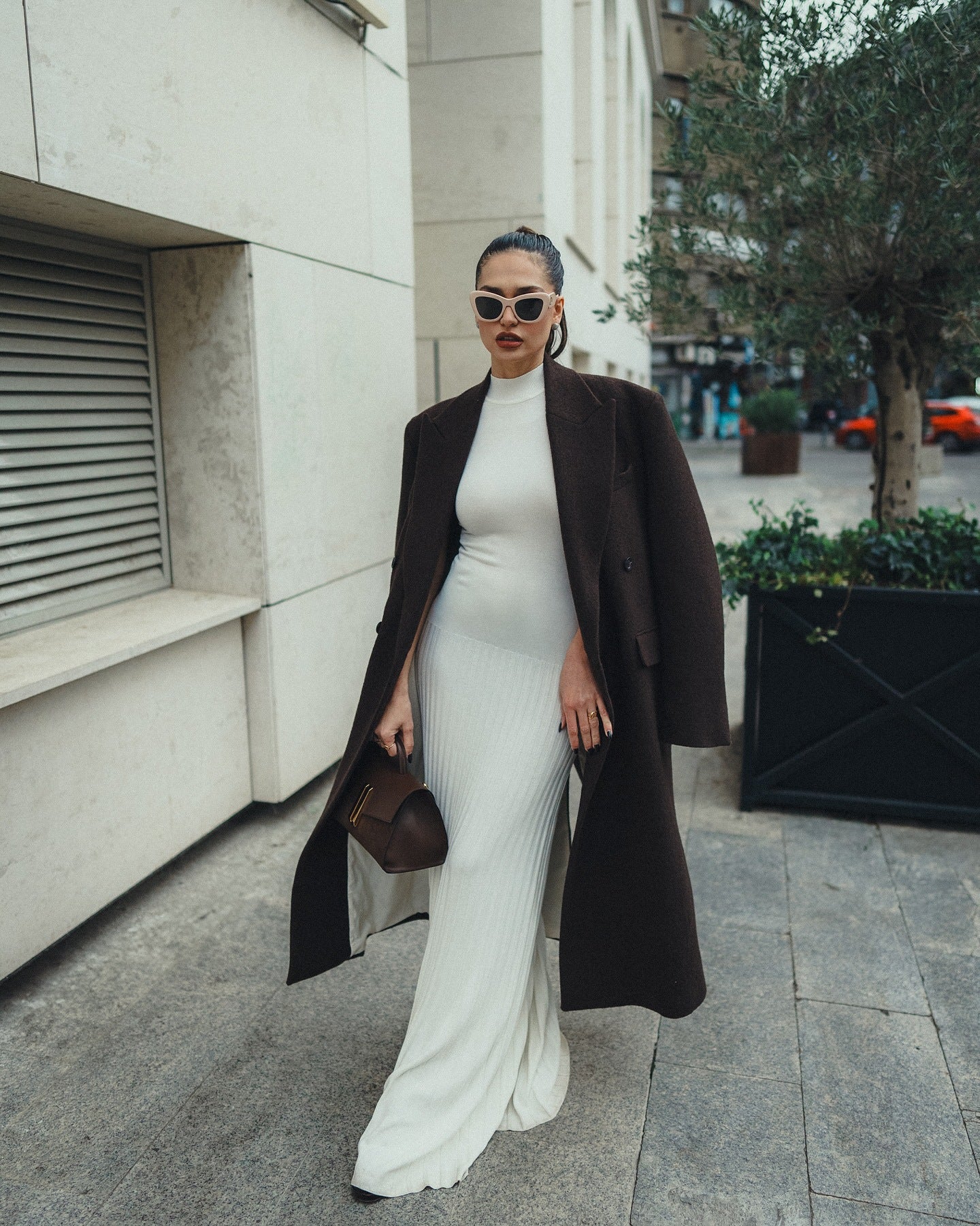 Elegant white bodycon maxi dress styled with a long black coat and sunglasses