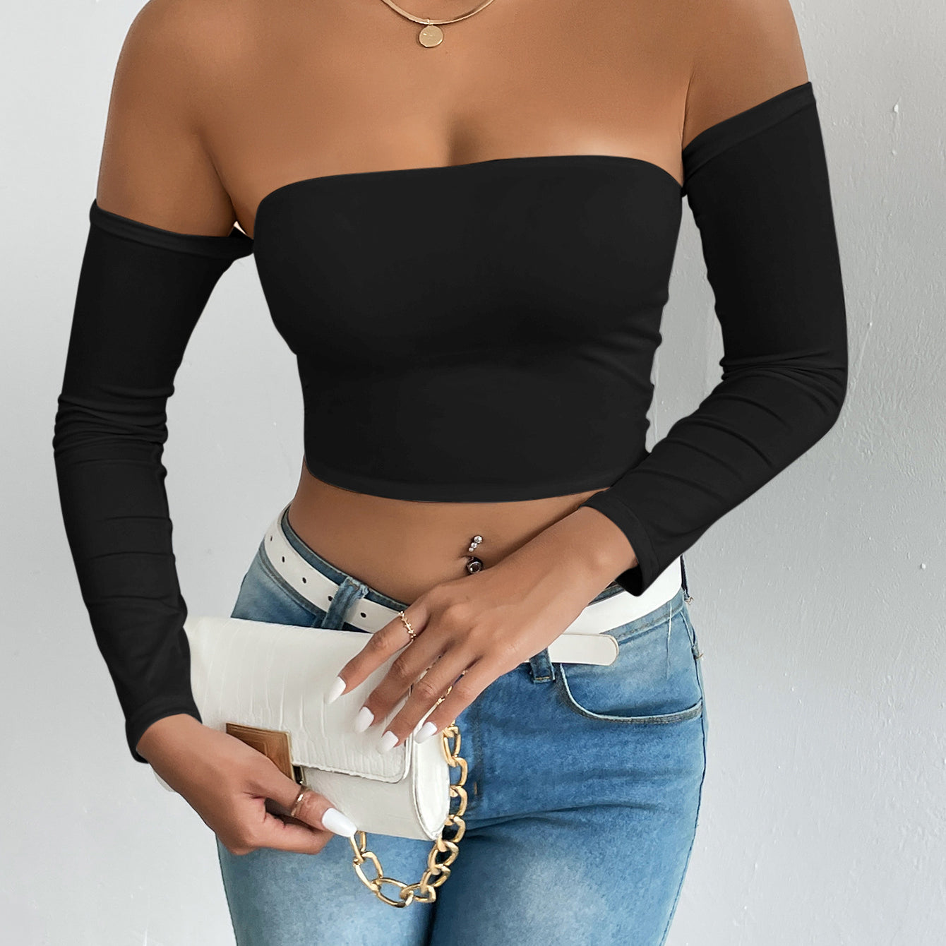Fashionable woman in black off-shoulder camisole with blue jeans and white handbag