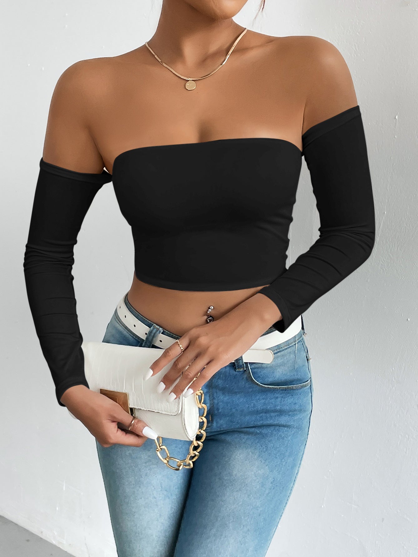 Fashionable woman in black off-shoulder camisole with blue jeans and white handbag