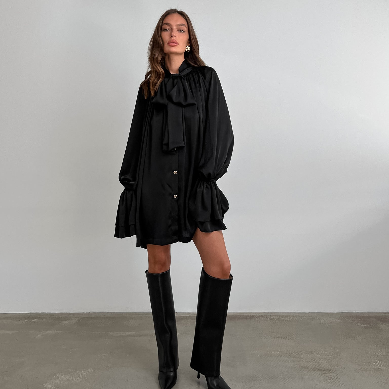 Black ruffled satin dress with long sleeves, styled with knee-high fashion boots