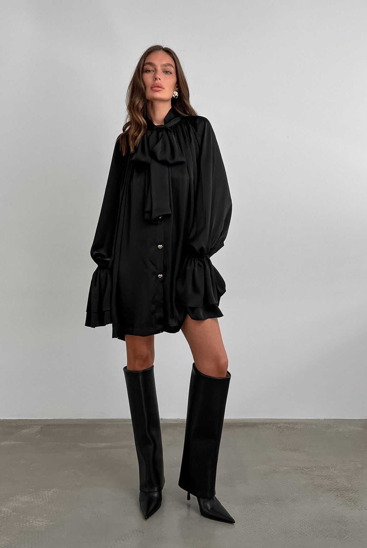 Black ruffled satin dress with long sleeves, styled with knee-high fashion boots