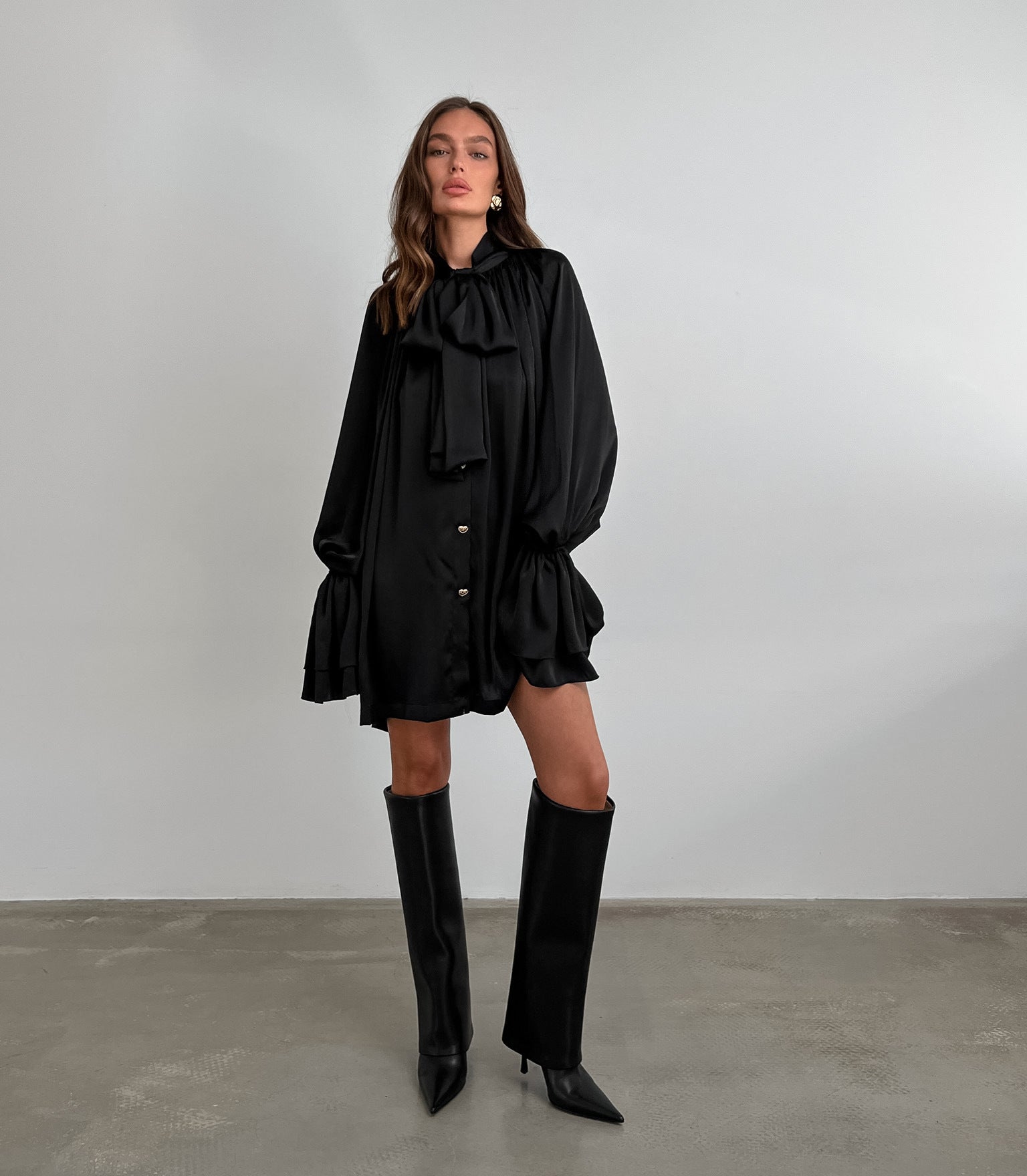 Black ruffled satin dress with long sleeves, styled with knee-high fashion boots