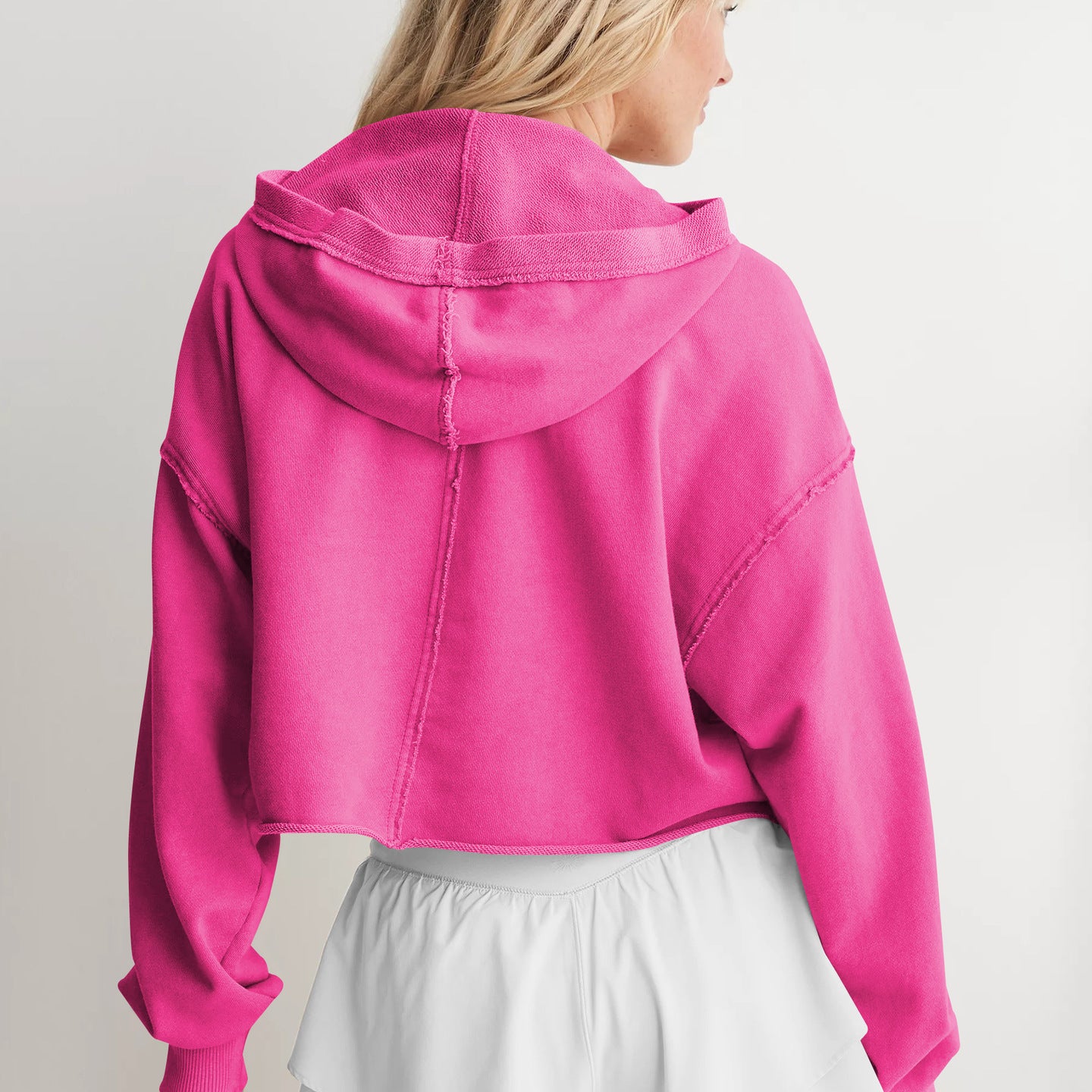 Hot pink cropped hoodie with dropped shoulders styled with white shorts, ideal for fashion enthusiasts