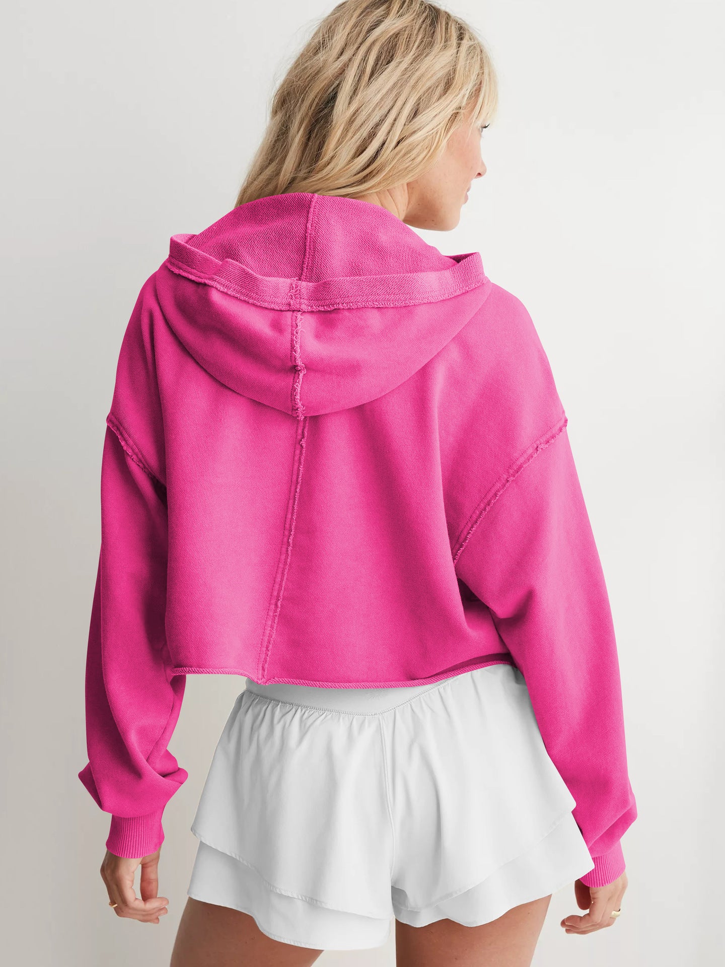 Hot pink cropped hoodie with dropped shoulders styled with white shorts, ideal for fashion enthusiasts